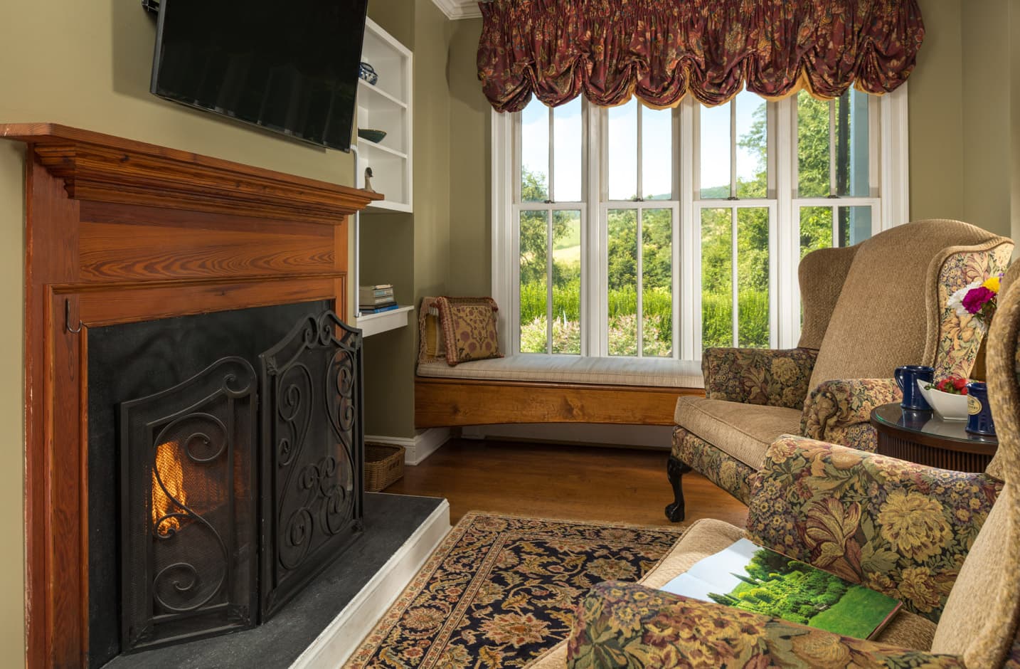 Two chairs facing a fireplace and TV with a wall of windows overlooking a garden