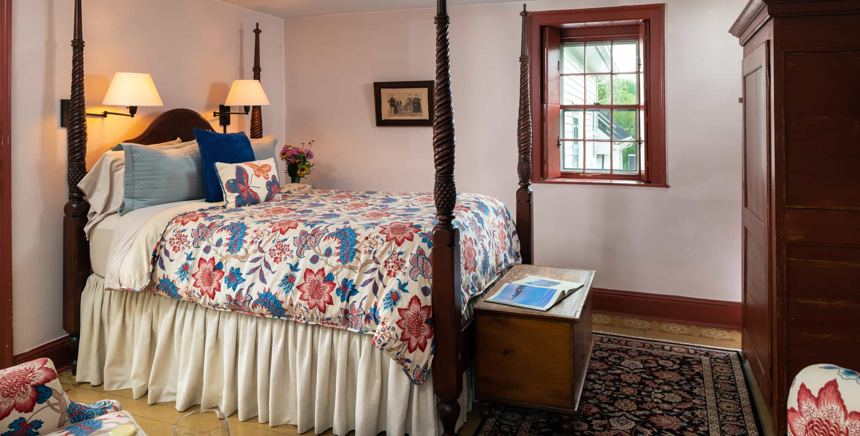 Four poster queen bed in a room with a window and a seating area for two