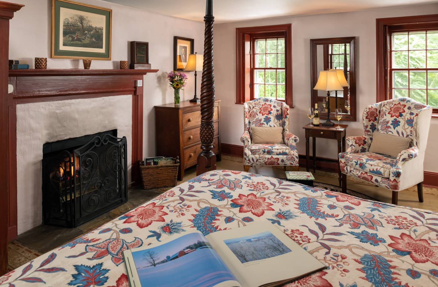 Four poster queen bed in a room with windows a seating area for two and a fireplace