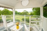 A covered patio with two Adirondack chairs and a small table overlooking a garden