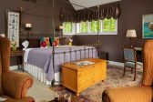 Wrought iron king bed in a room with dark brown walls, and a chest at the foot of the bed and a seating area