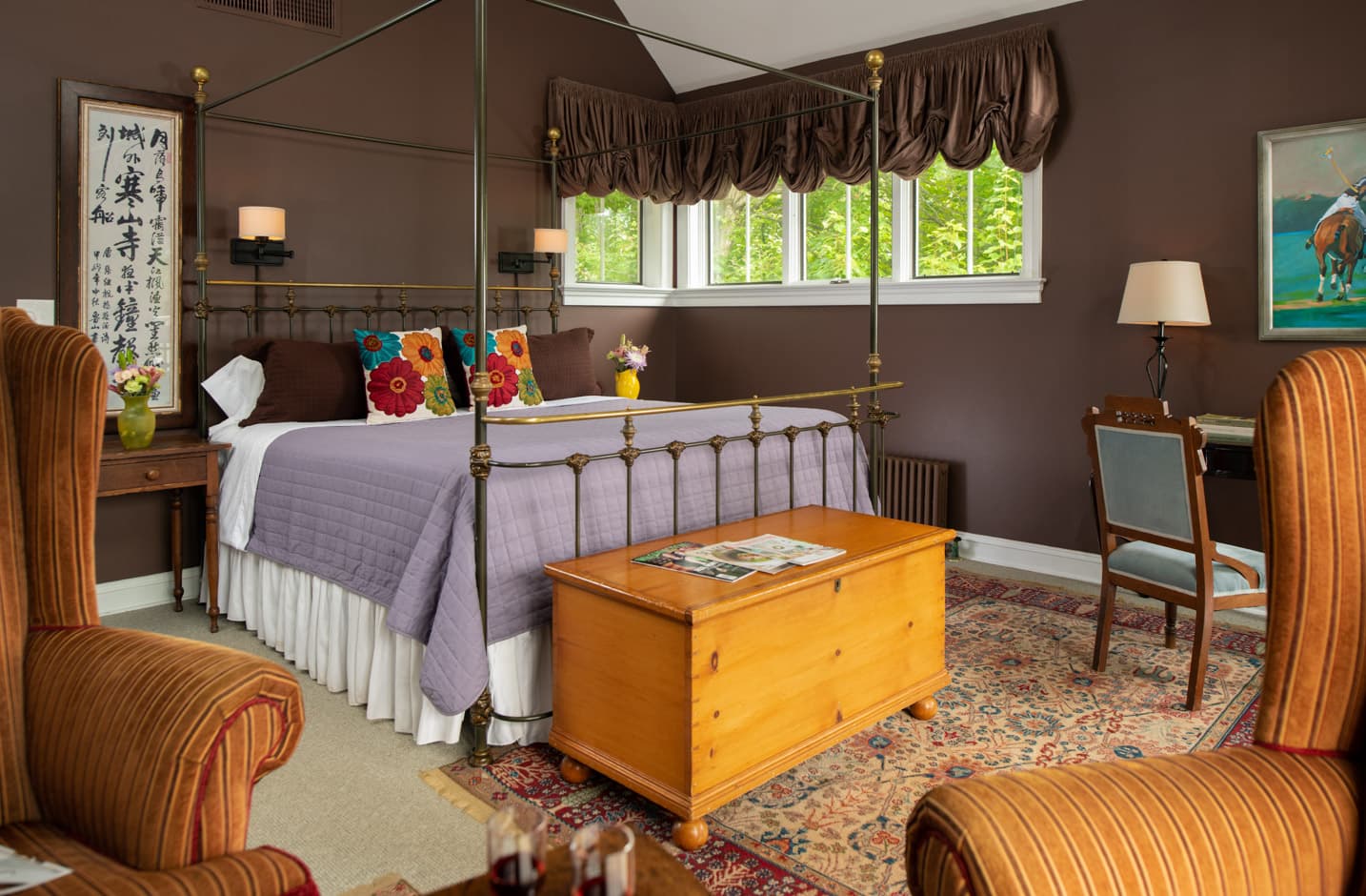 Wrought iron king bed in a room with dark brown walls, and a chest at the foot of the bed and a seating area