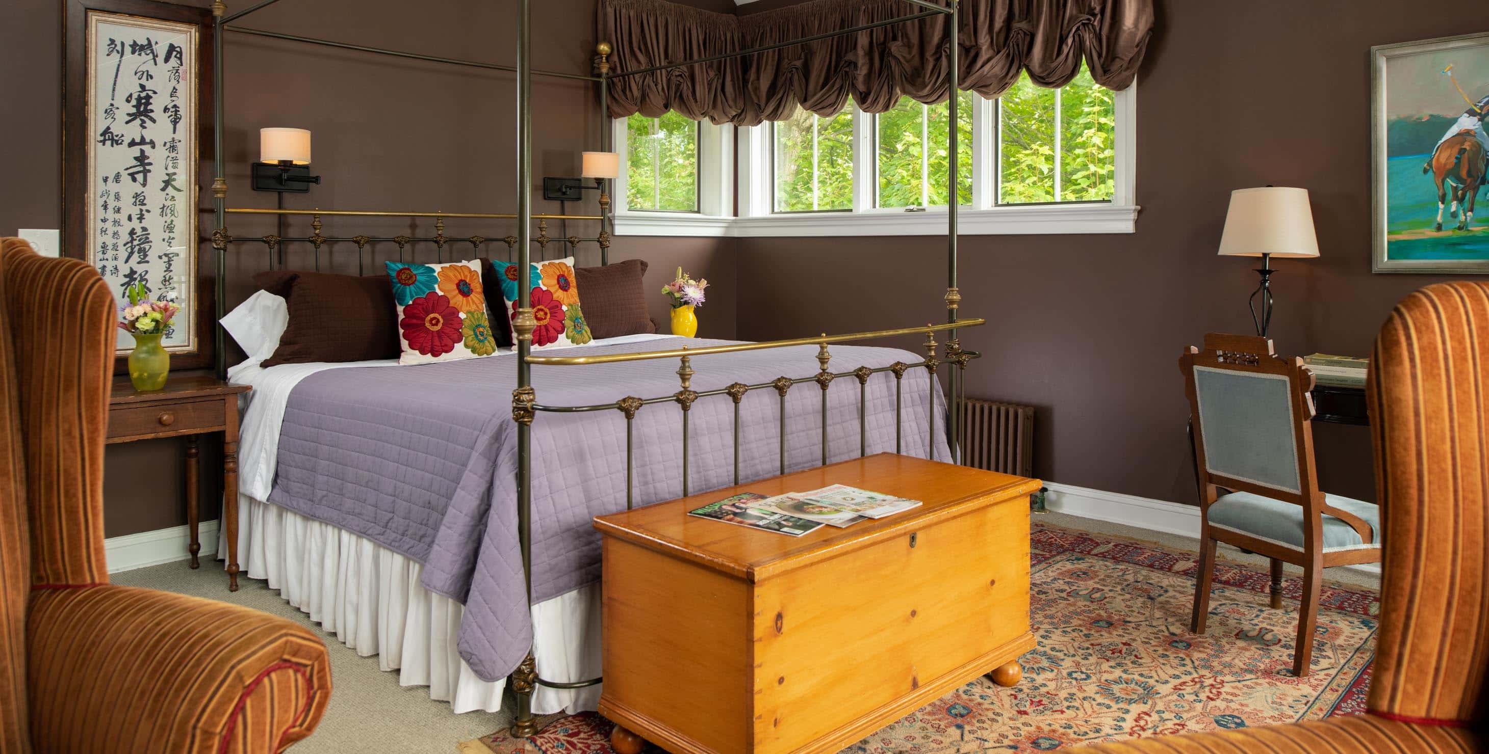 Wrought iron king bed in a room with dark brown walls, and a chest at the foot of the bed and a seating area