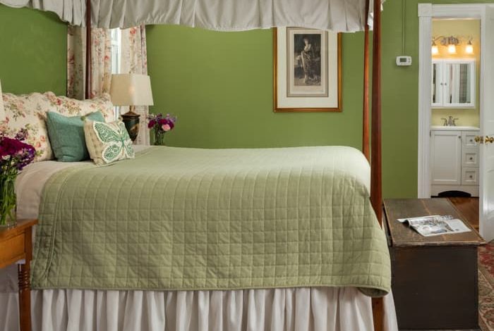 Canopied four-poster queen bed with a green blanket in a room with hardwood floors