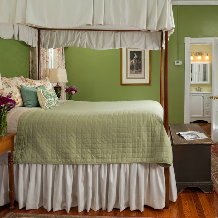 Canopied four-poster queen bed with a green blanket in a room with hardwood floors