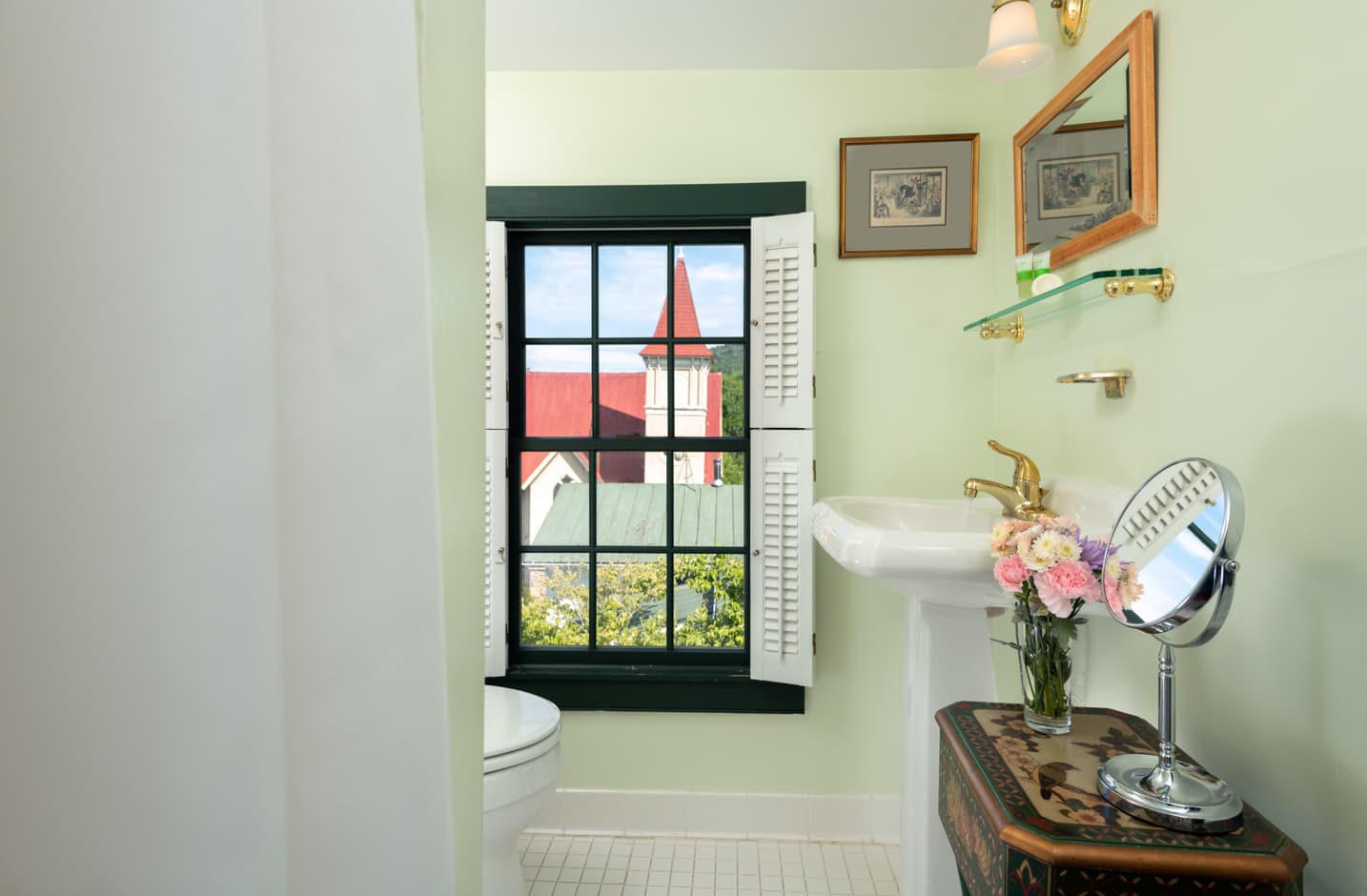 A bathroom with a shower and tub combo, sink and a window with a view of the chapel