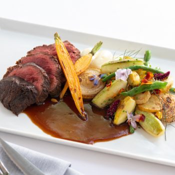 Beef served with seasonal vegetables and a glass of red wine